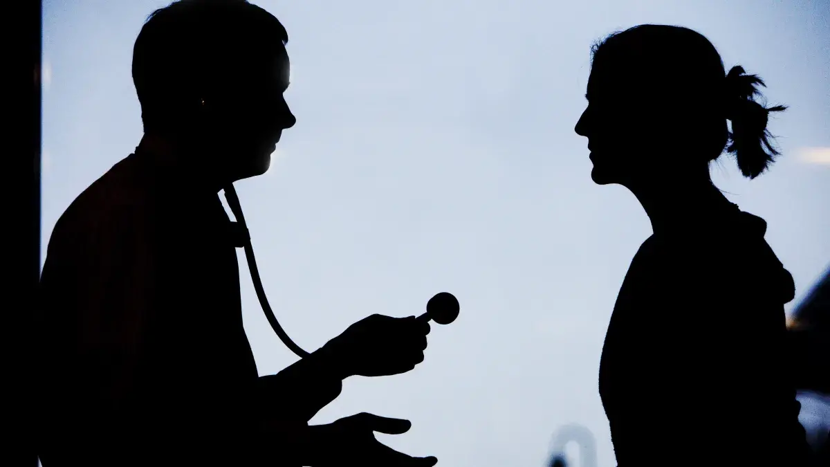 the silhouettes of two people looking at each other. One person is holding a stethoscope.