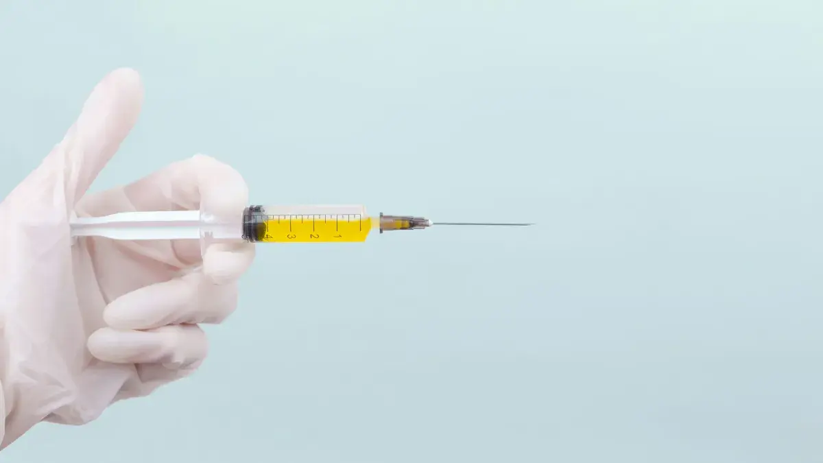 A hand wearing a medical glove holding a syringe full of yellow liquid