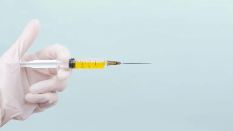 A hand wearing a medical glove holding a syringe full of yellow liquid