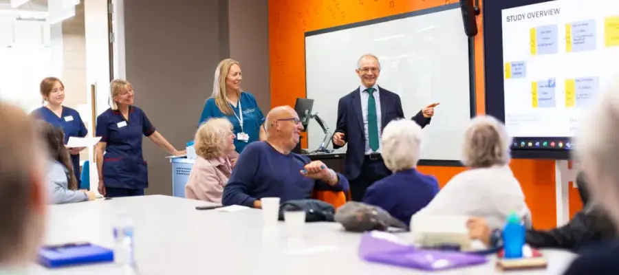 Boardroom with Adam Hill presenting to a room, and patients and nurses are there