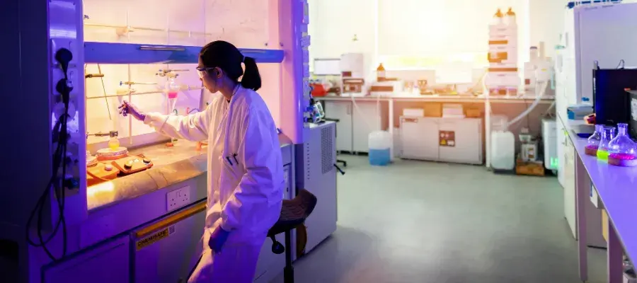 researcher wearing a lab coat and goggle working under a hood with chemicals
