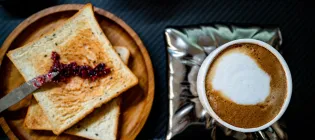 A top-down view of two pieces of toast with jam on a wooden plate, and a cup of milky coffee