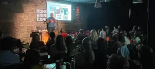 Rob Illingworth on a stage presenting to a large audience in a darkened room 