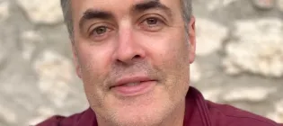 Professor Donal O'Carroll is smiling at the camera, wearing a red shirt in front of a stone wall