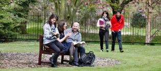 three students chatting on a park bench, two students walk up the path towards them