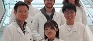 Wei-Yu Lu and is five lab members smiling in the internal IRR staircase in the lab, with their lab coats