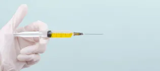 A hand wearing a medical glove holding a syringe full of yellow liquid