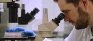 Scientist looking down a microscope and holding well-plate
