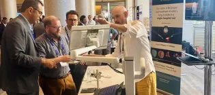 Members of Prothea are standing in discussion, whilst looking at a screen at a conference stall