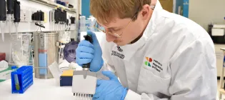 Researcher pipetting something in a lab in a white lab coat