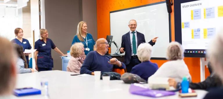 Boardroom with Adam Hill presenting to a room, and patients and nurses are there