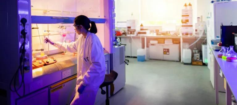 researcher wearing a lab coat and goggle working under a hood with chemicals