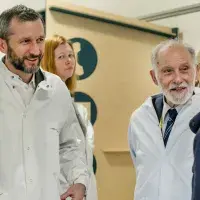 Three adults wearing lab coats on a facility tour