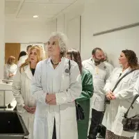A dozen adults wearing lab coats on a facility tour