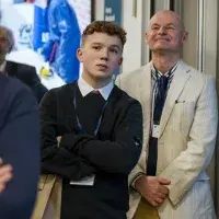 A student stands in a crowd listening to an unseen public speaker