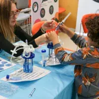 Child playing with small hand-held bioreactor, being shown how to do it by volunteer