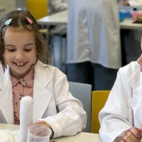 Two girls looking and smiling at a test tube that's bubbling over