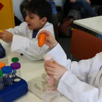 Two boys at a table putting liquid into a test tube that's overflowing with foam