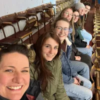 a group of people sat in a line in stadium seating, smiling at the camera