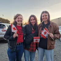 Three people standing outside in a car park, all holding small Canadian flags