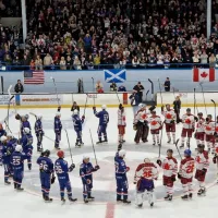 two ice hockey teams standing on the ice in a large circle with their sticks raised in the air.
