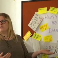 Facilitator in front of board of post-it notes, titled 'human by design'