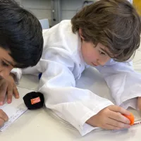 Two boys at a table, one writing in a notebook, another studying the tube of balls/immune cells