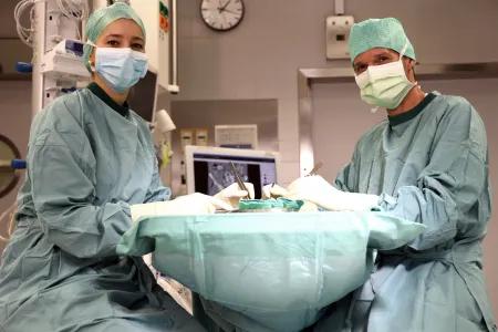 Two surgeons working on an operating table, looking at the camera.
