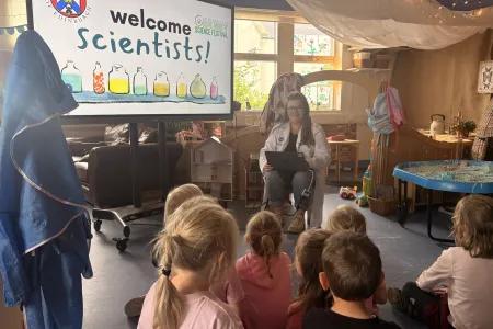 A researcher sitting on a low chair in front of a classroom of children