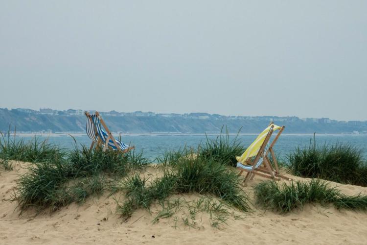 Two deck chairs on a grassy sandy beach on an overcast day