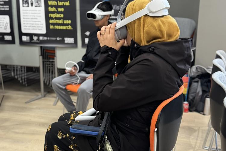 A boy and woman sit down in a hall with VR headsets and a poster behind titled FishEye Reality