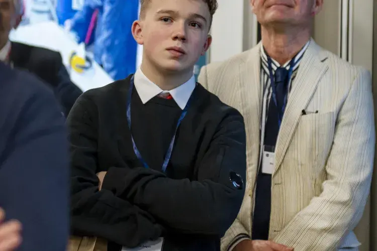 A student stands in a crowd listening to an unseen public speaker