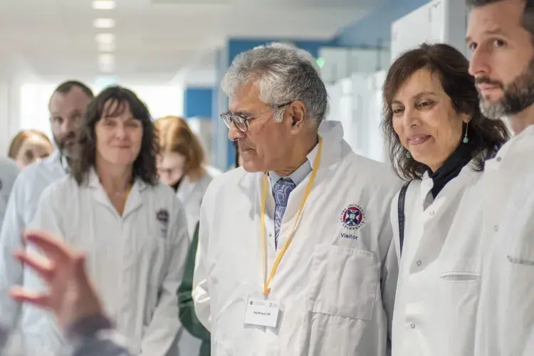 A dozen adults wearing lab coats on a facility tour