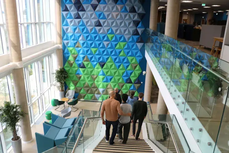 Public walking down internal staircase with green/blue colourful wall in background
