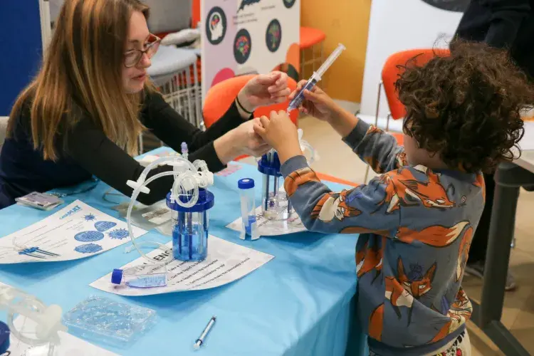 Child playing with small hand-held bioreactor, being shown how to do it by volunteer
