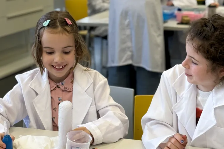 Two girls looking and smiling at a test tube that's bubbling over