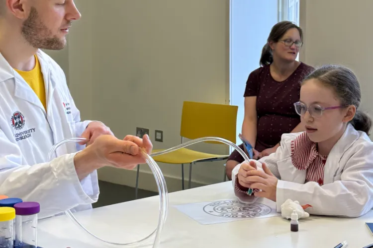 A girl holding a tube with small silver and red beads inside 