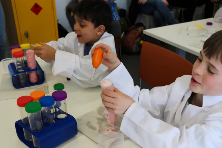 Two boys at a table putting liquid into a test tube that's overflowing with foam