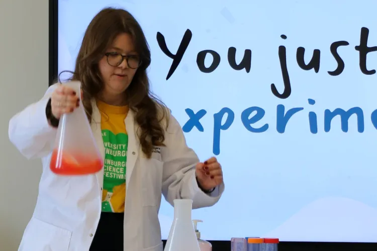 Lucy holding a giant conical flask with bright orange liquid inside that's smoking