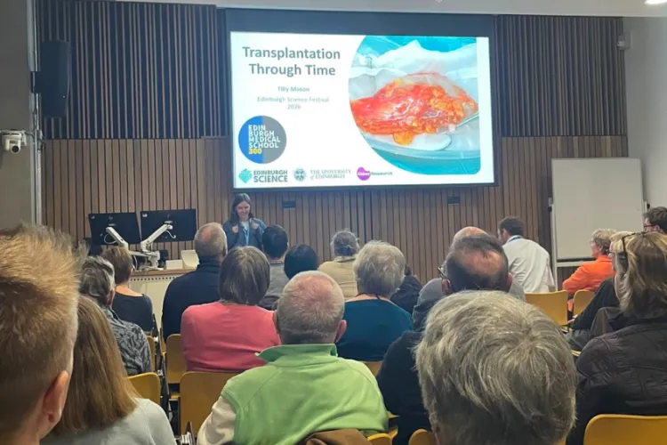 Tilly Mason at the front of the room presenting with the photo being taken at the back of the room, with backs of heads in shot