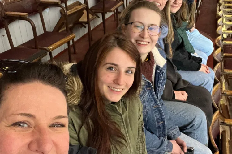 a group of people sat in a line in stadium seating, smiling at the camera