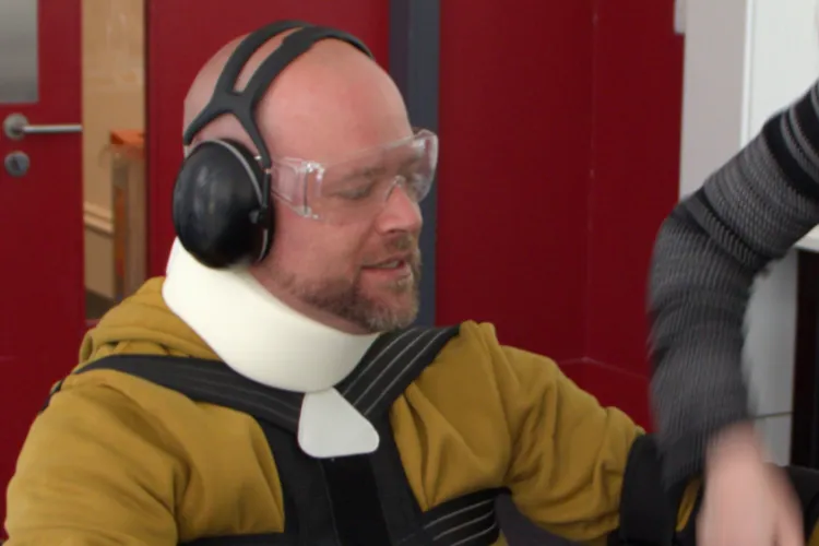 Someone wearaing neckbrace, headphones and a low-mobility suit