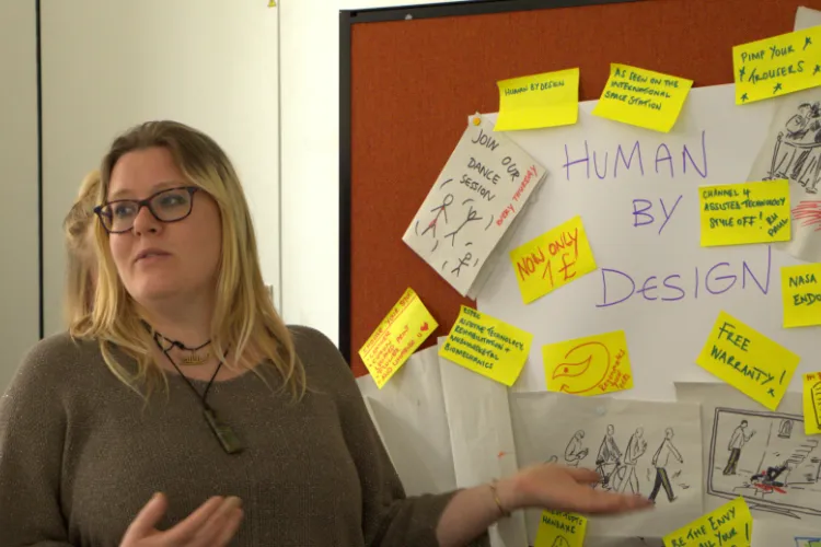 Facilitator in front of board of post-it notes, titled 'human by design'