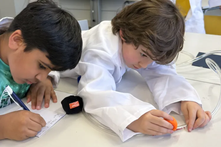 Two boys at a table, one writing in a notebook, another studying the tube of balls/immune cells