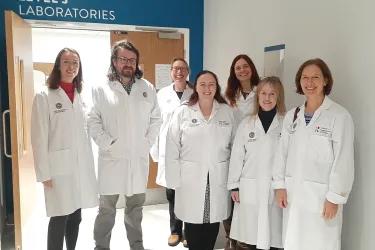 Joy and seven members of SPICe standing in lab coats within IRR