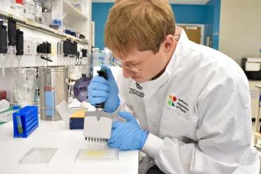Researcher pipetting something in a lab in a white lab coat