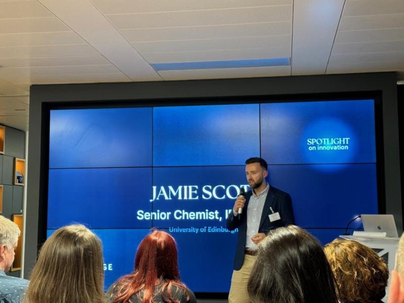 Jamie Scott speaking into a microphone in a seminar room, giving a presentation.