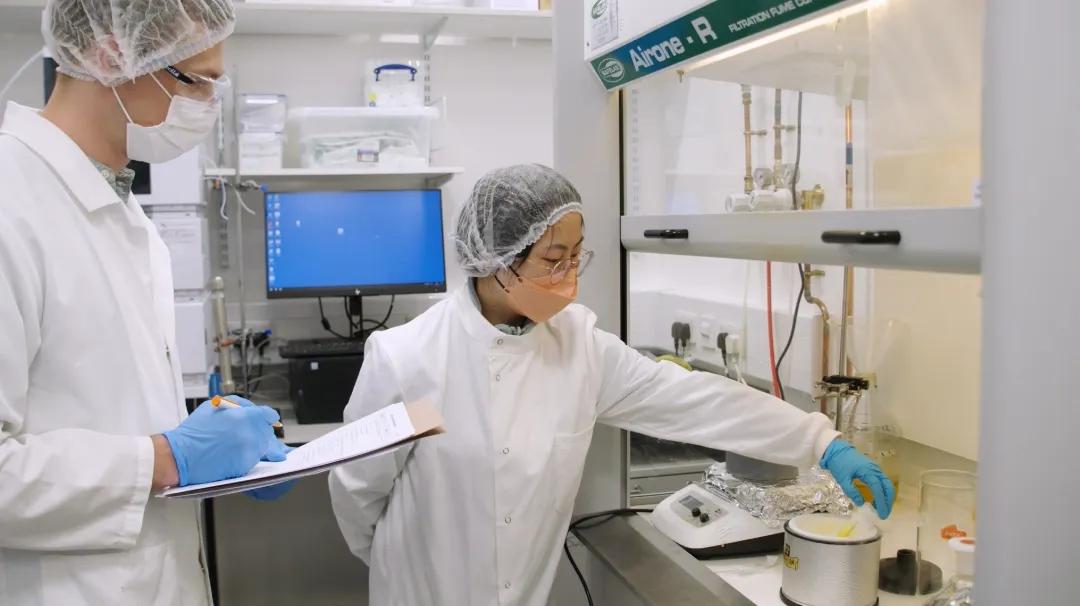 Two researchers with face masks on doing research in fume hood