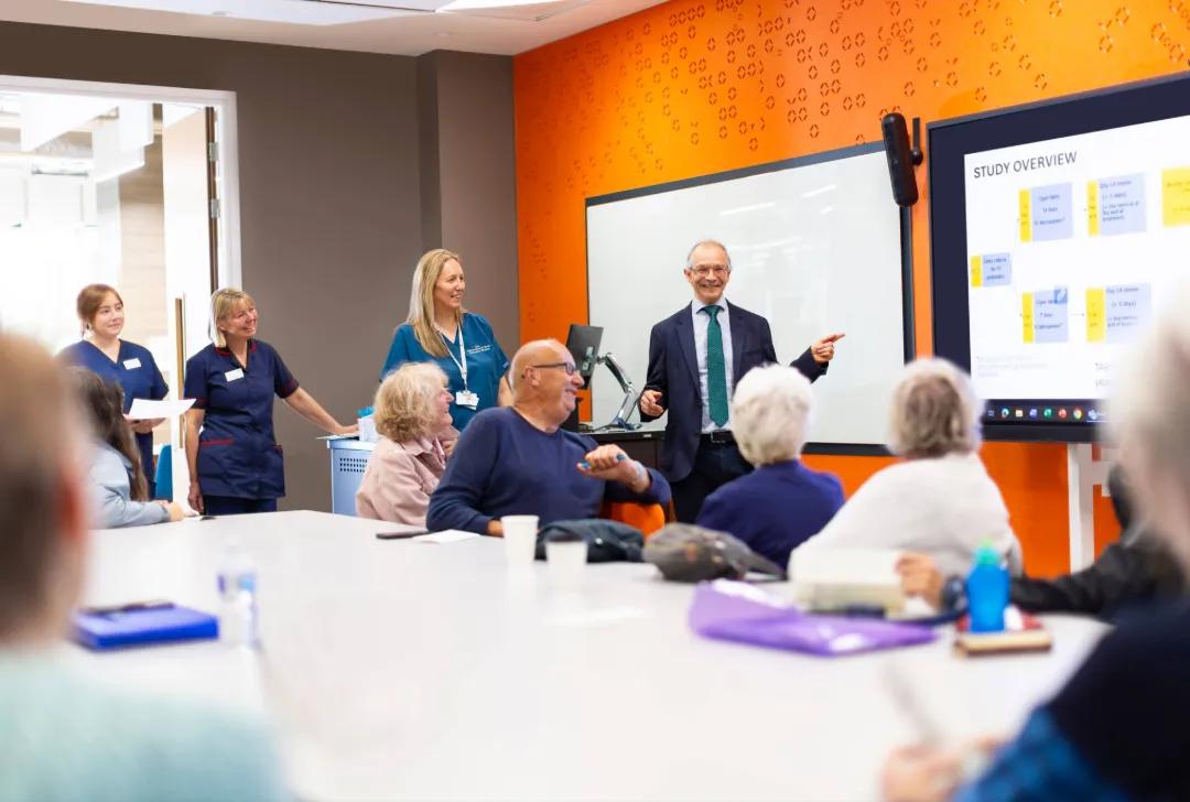 Boardroom with Adam Hill presenting to a room, and patients and nurses are there