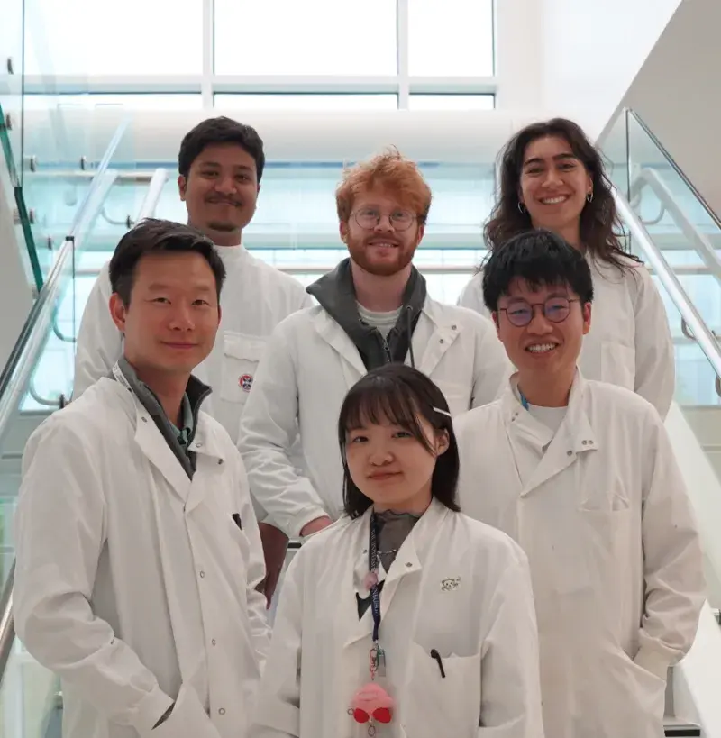 Wei-Yu Lu and is five lab members smiling in the internal IRR staircase in the lab, with their lab coats